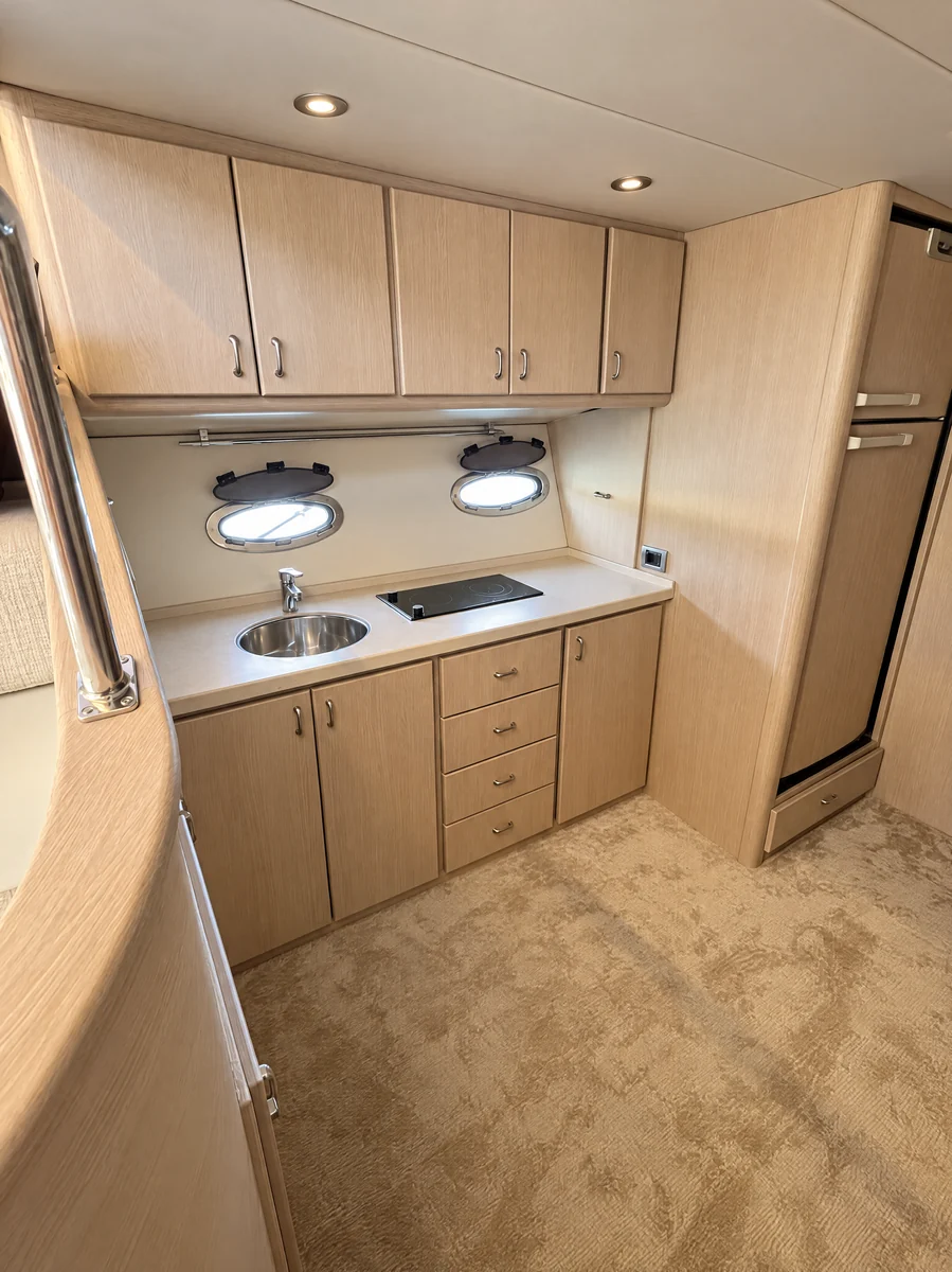 The galley from the stairs: worktop, round sink, hob, two portholes and the tall fridge at its end